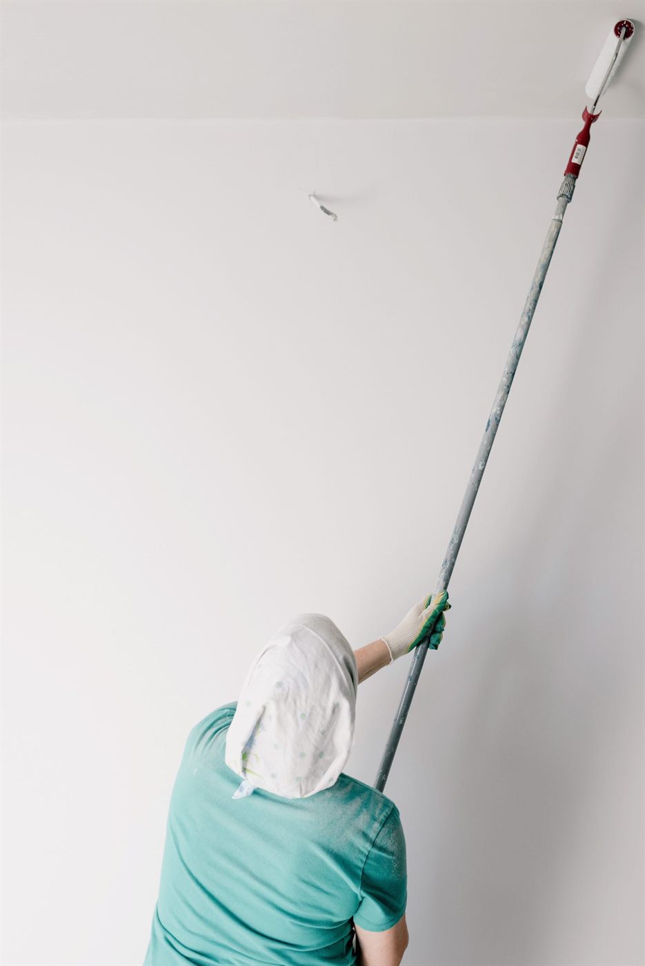 Schilder werkt een plafond af met een verfroller op een verlengsteel