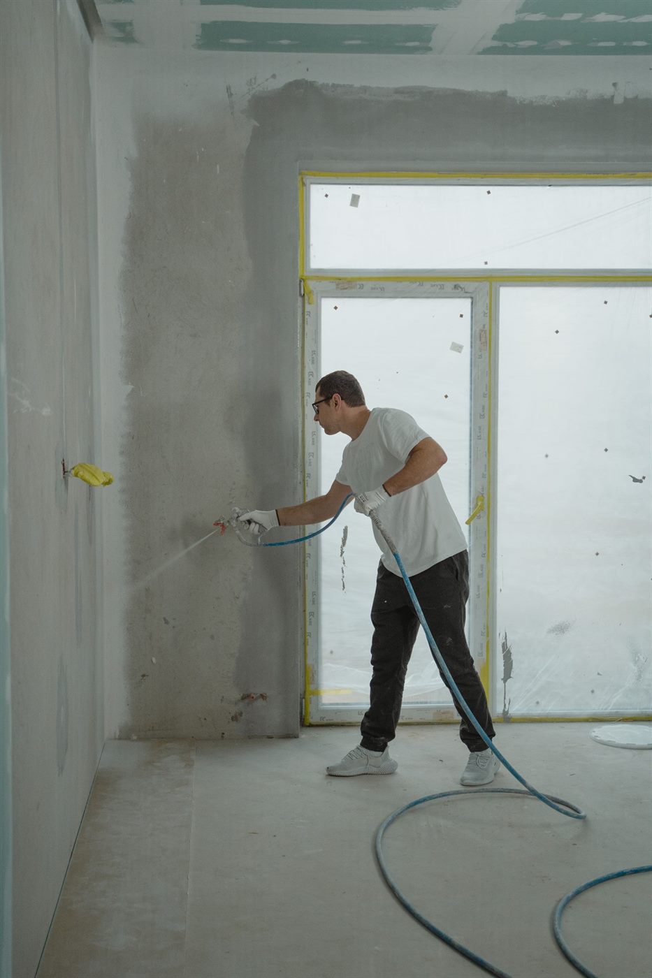 Vakman spuit een wand met een spuitinstallatie onder hoge druk